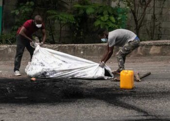 epa10605579 Two men cover the cremated body of a person in Port-au-Prince, Haiti, 02 May 2023. At least five people were killed on 02 May 2023 by the population in Petion-ville, Port-au-Prince, for being alleged members of the Ti Makak armed group, dismantled a few weeks ago by the National Police.  EPA/Johnson Sabin